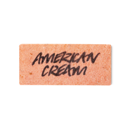 A peachy pink, rectangular washcard, consisting of apple pulp, with 'American Cream' written across it in black Lush writing.